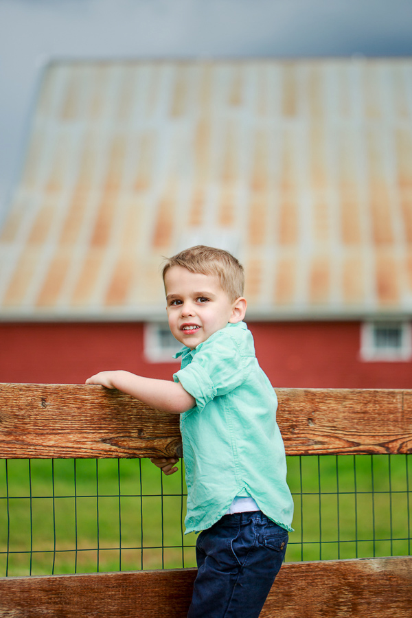 a little boy climbing the fence with a red barn in the background