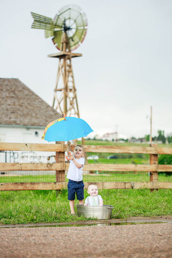 a little boy holding an umbrella open over his baby brother in the park