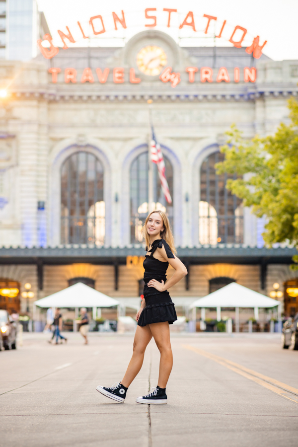 A girl in a black dress while standing in the middle of the street in front of Union Station