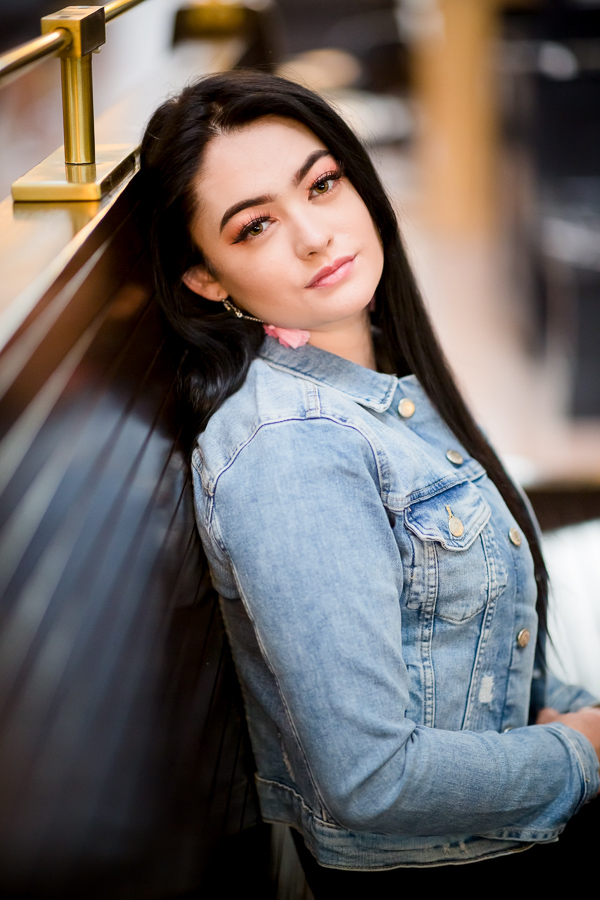 A girl with long and straight black hair sitting back on a bench